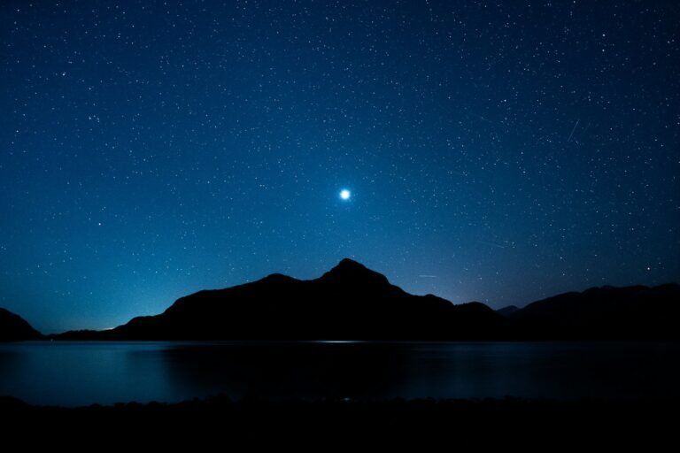 Stars twinkle above mountains and water.