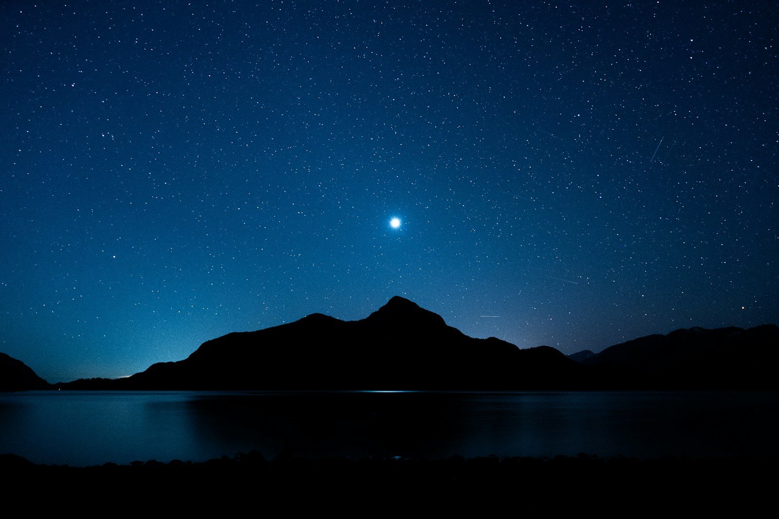 Stars twinkle above mountains and water.